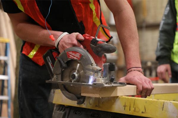 A student using a hand saw to cut wood.